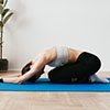 A girl dressed in sports equipment is exercising the balasana pose on a blue fitness mat.
