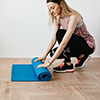 A girl in a squatting posture is preparing the fitness mat on the floor to do exercises fast.