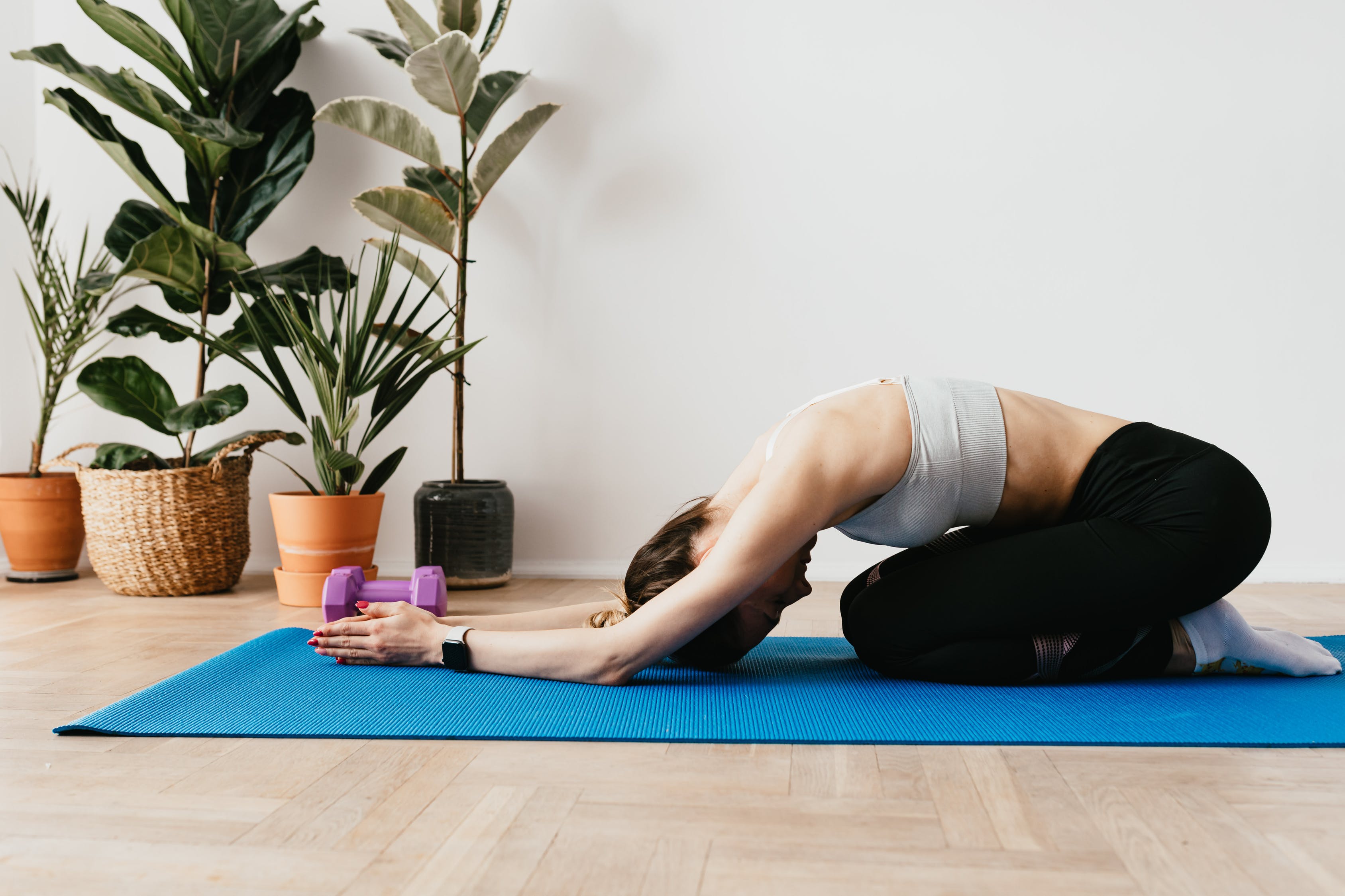 A fitness model, clad in athletic attire, demonstrates the Balasana pose on a blue fitness mat.