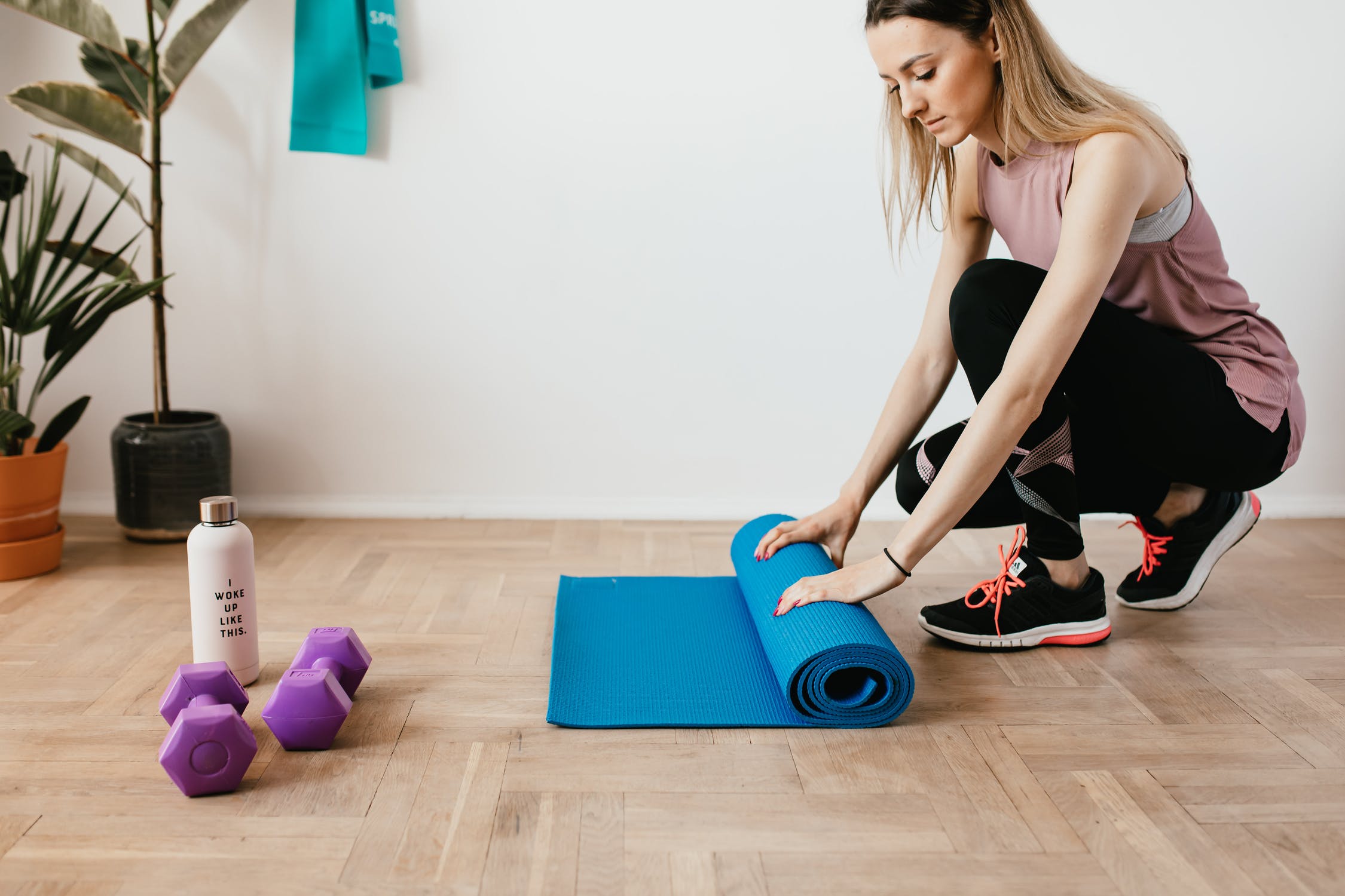 A girl in a squatting posture is preparing the fitness mat on the floor to do exercises fast.
