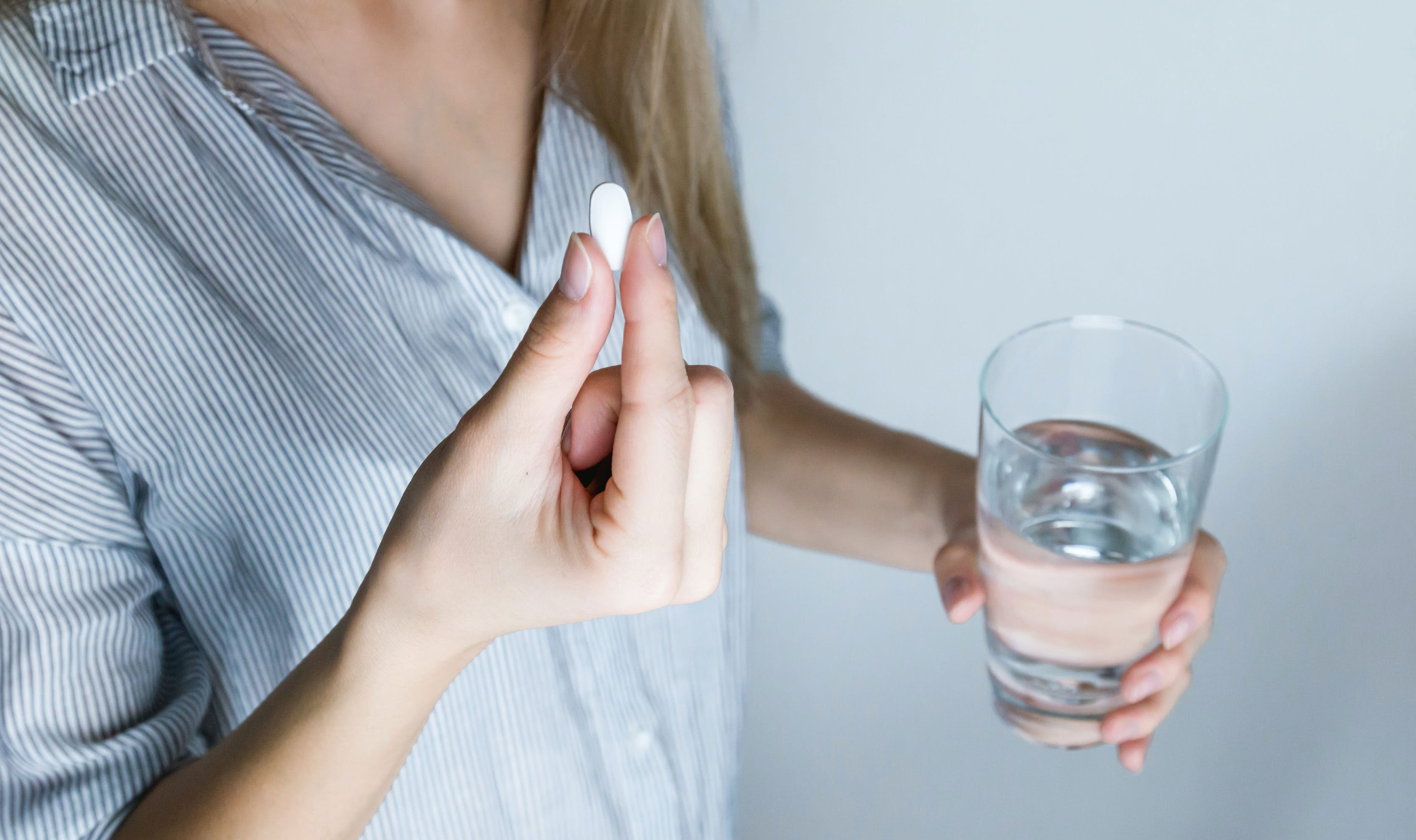 A person's hand holds a pill, illustrating treatment for constipation symptoms.